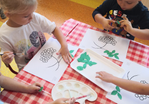 dzieci przy stoliku naklejają na kartkę listki jarzębiny we wskazanym miejscu